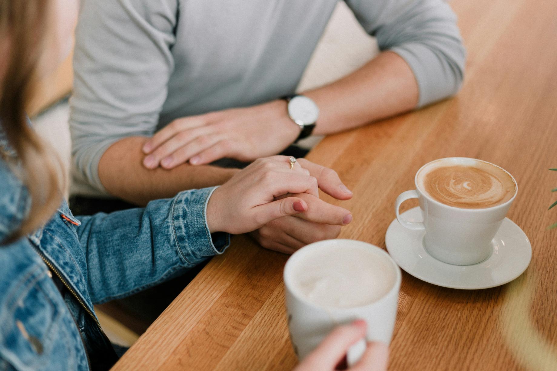 two adults holding hands and drinking coffee