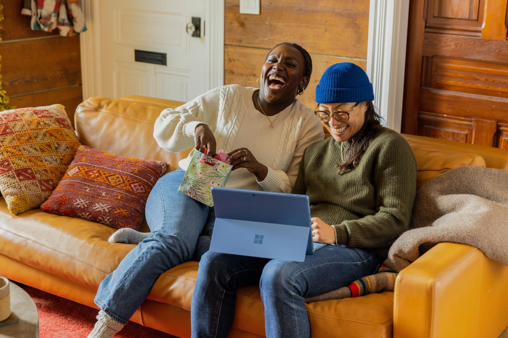 two people laughing together while knitting and looking at a laptop